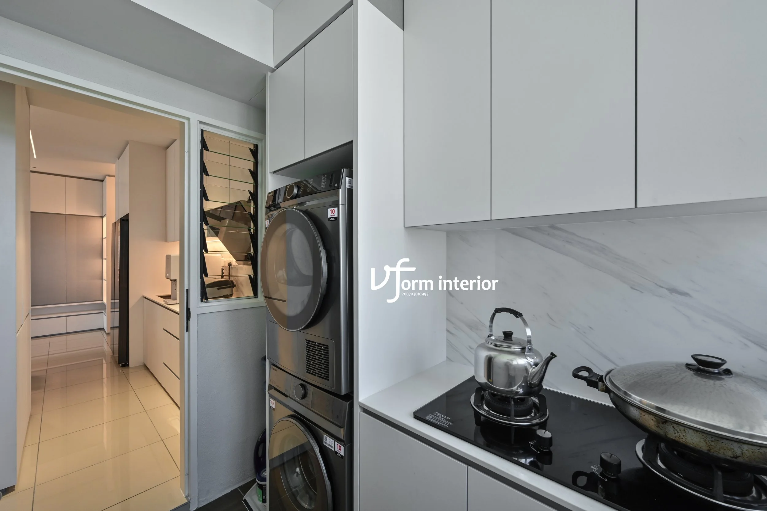 Modern kitchen with gray cabinets, a gas stove with a teapot and a pot, white marble backsplash, and a laundry area with stacked washing machine and dryer in the background.
