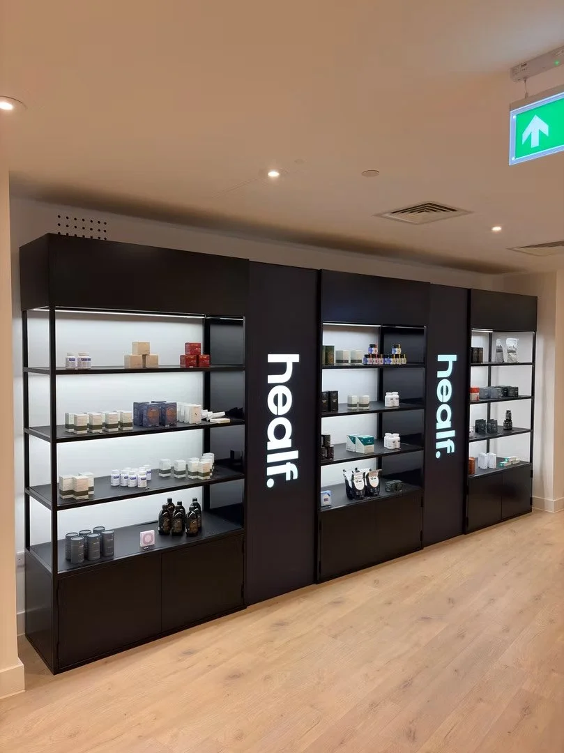 Black display shelves with various health and wellness products arranged on the shelves, in a store or clinic setting, with the word 'healr' illuminated on the side panels.