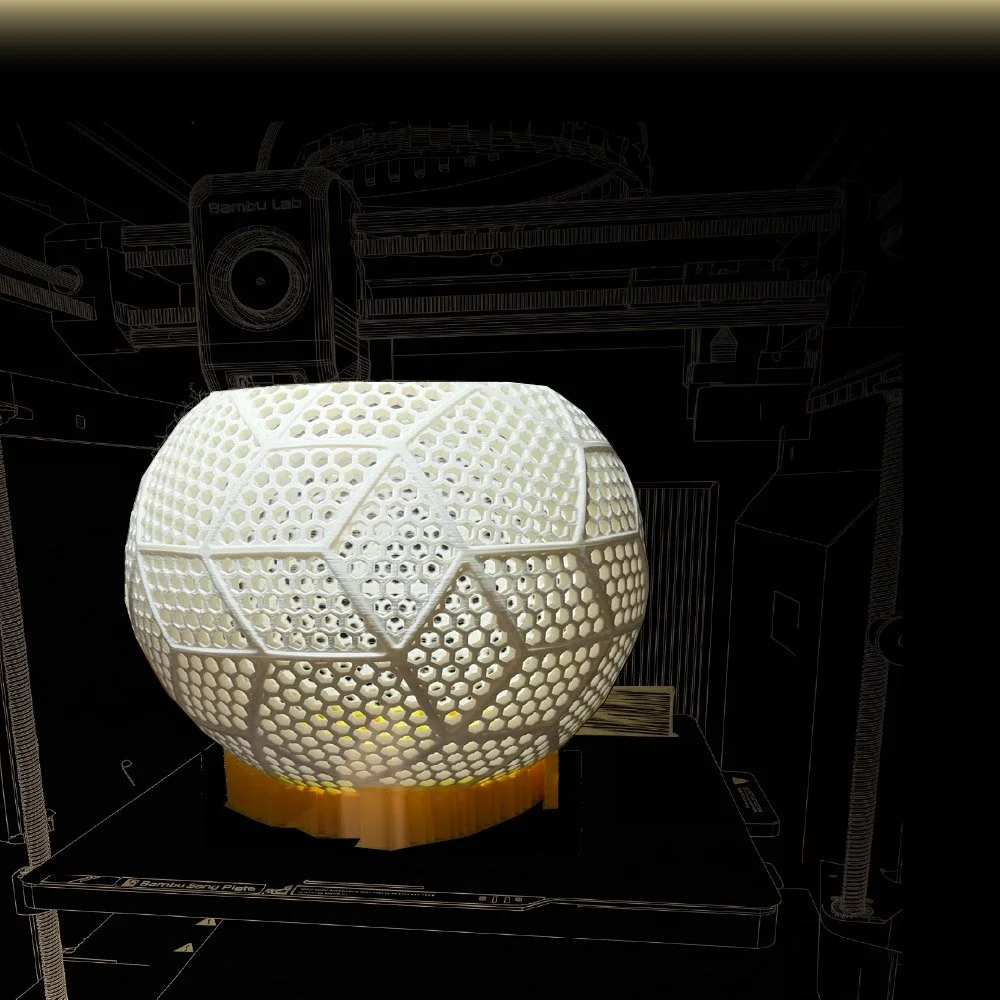 A 3D printed geometric sphere with a honeycomb pattern, sitting on a yellow base, with a black background and white wireframe overlay of the 3D printing environment.