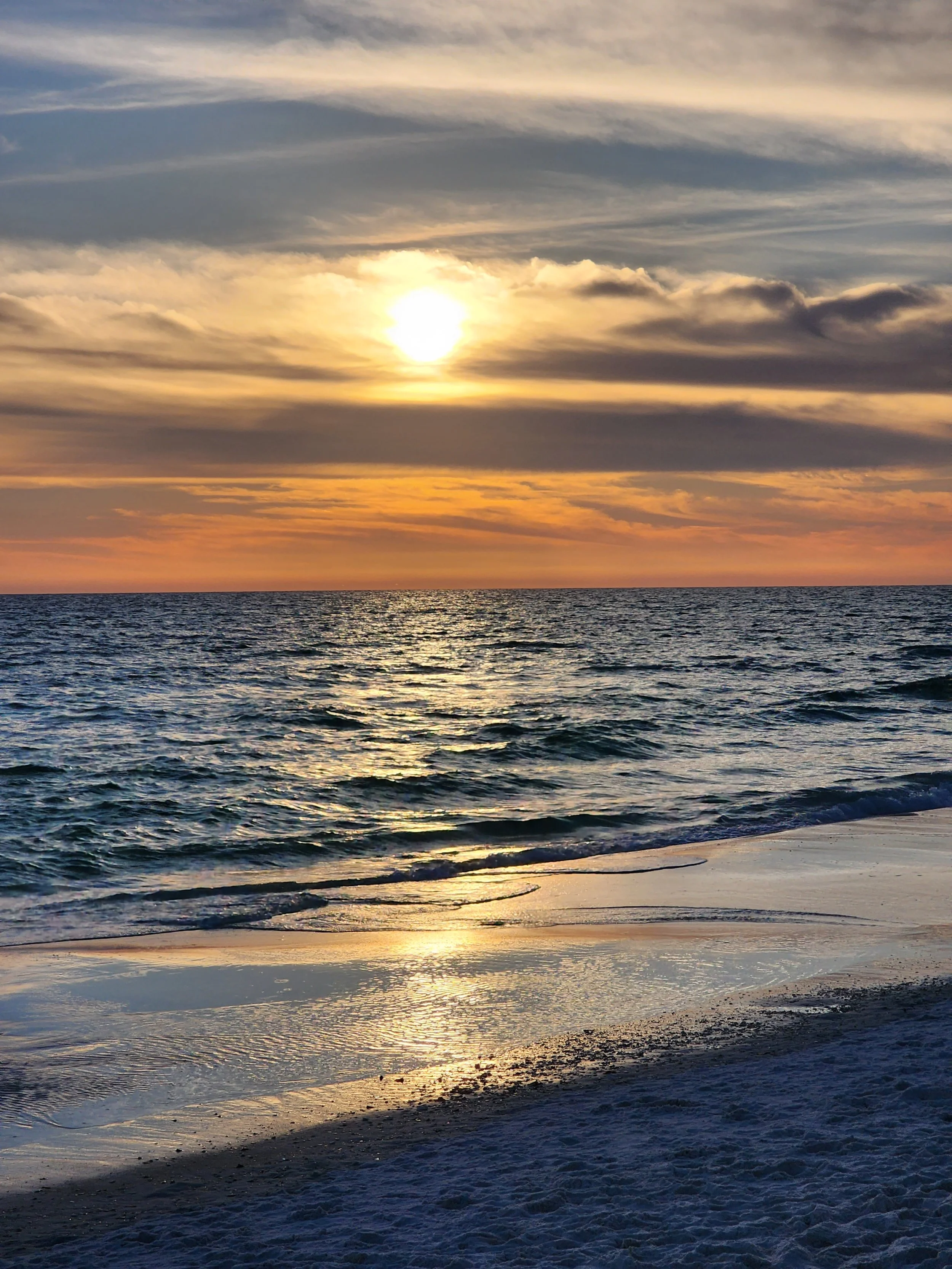 Sun setting over the ocean with a cloudy sky and waves crashing on the beach