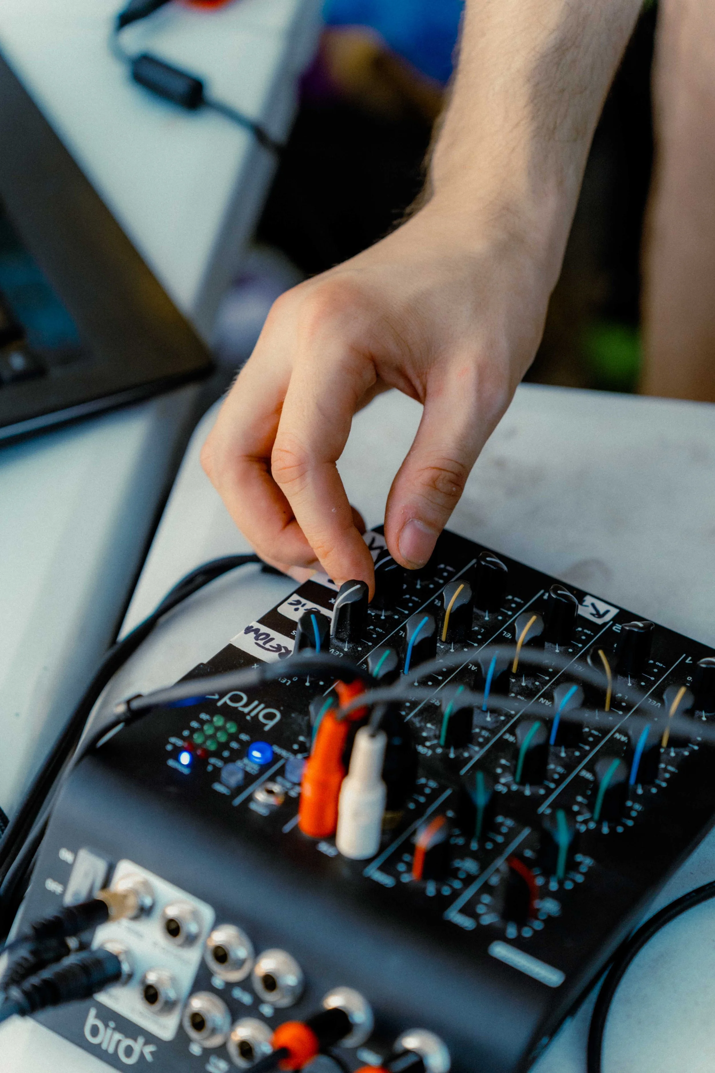 Main d'ajustant un synthétiseur connecté à un mélangeur audio avec plusieurs câbles colorés.