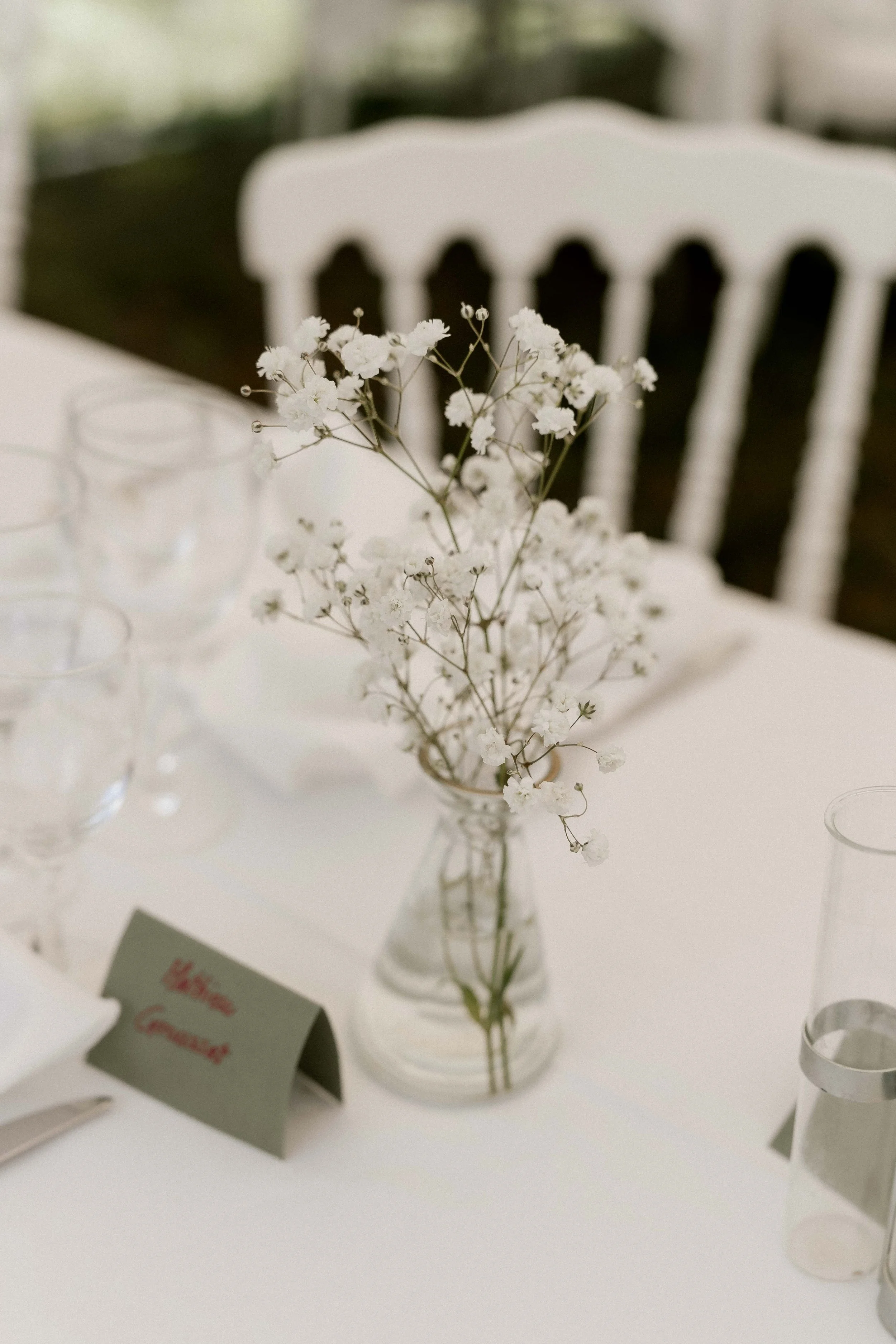 Une vase avec des fleurs blanches délicates sur une table blanche, avec un fond flou et une étiquette dans un endroit visible.