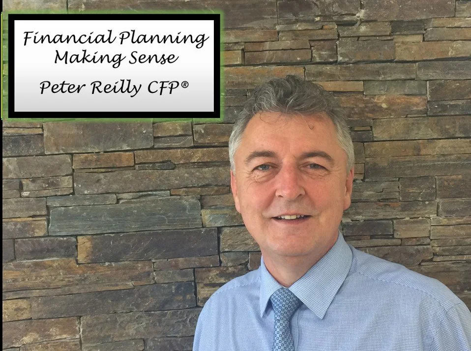 A man in a light blue dress shirt and patterned tie standing in front of a stacked stone wall, smiling, with a sign that reads "Financial Planning Making Sense, Peter Reilly CFP" in the top left corner.