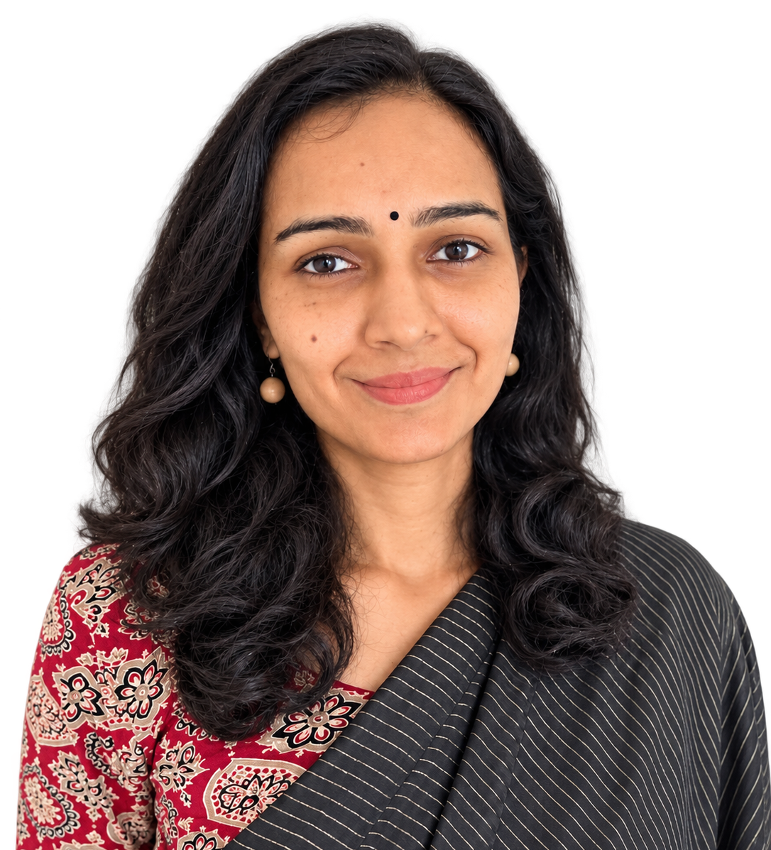 A woman with dark, curly hair wearing a black and gold sari with a red and gold patterned blouse, smiling softly.