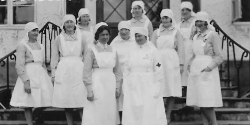 En gruppe sykepleiere i uniformer foran en bygning, tatt i svart-hvitt.