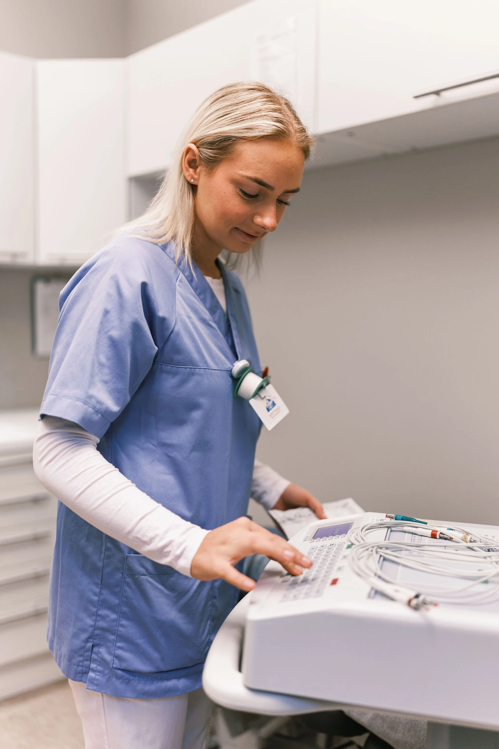 En ung kvinne iført medisinsk uniform som bruker en medisinsk enhet på et arbeidsbord i et klinikkmiljø.