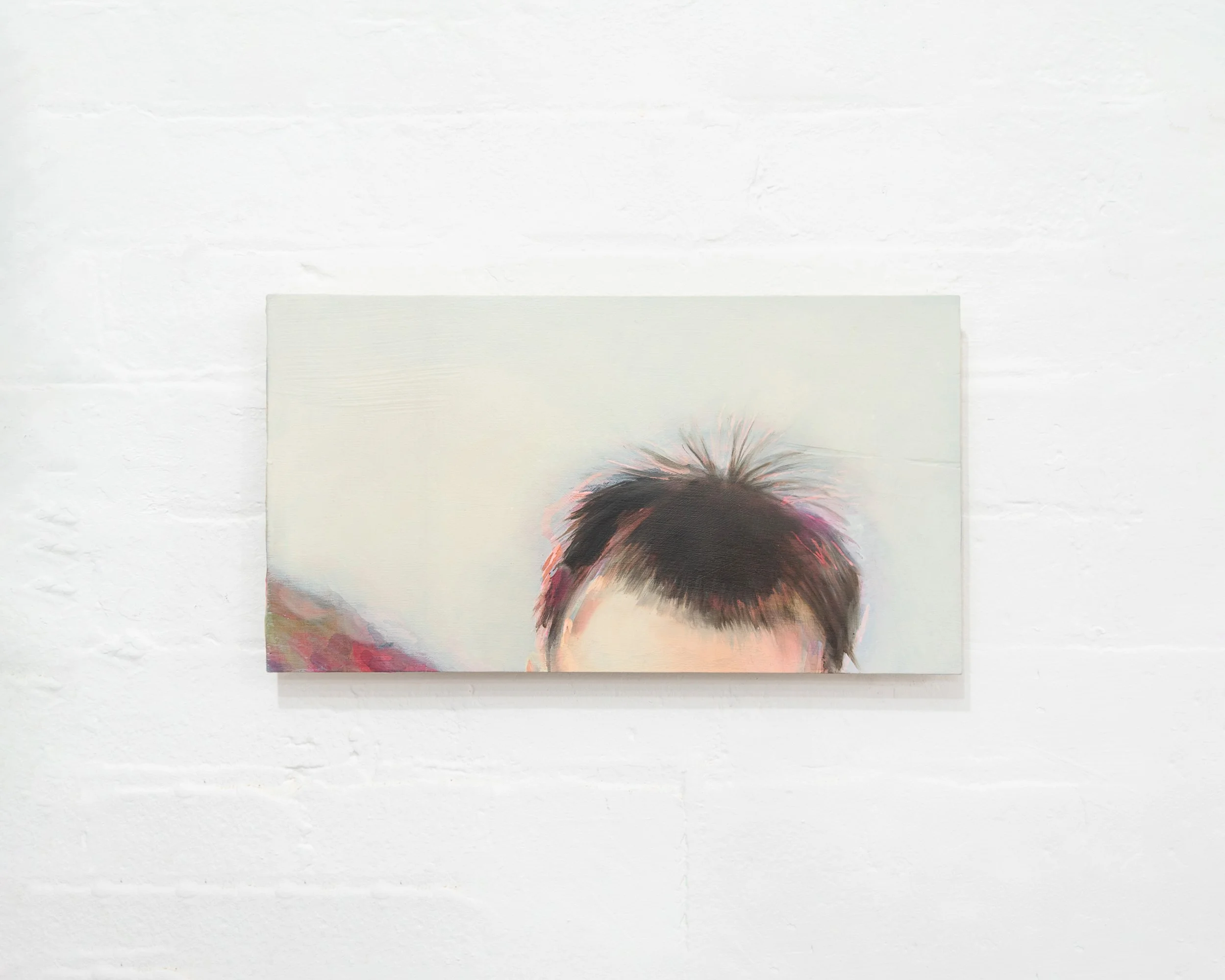 Close-up of a colorful portrait painting of a person's head with dark, spiky hair, mounted on a white textured wall.