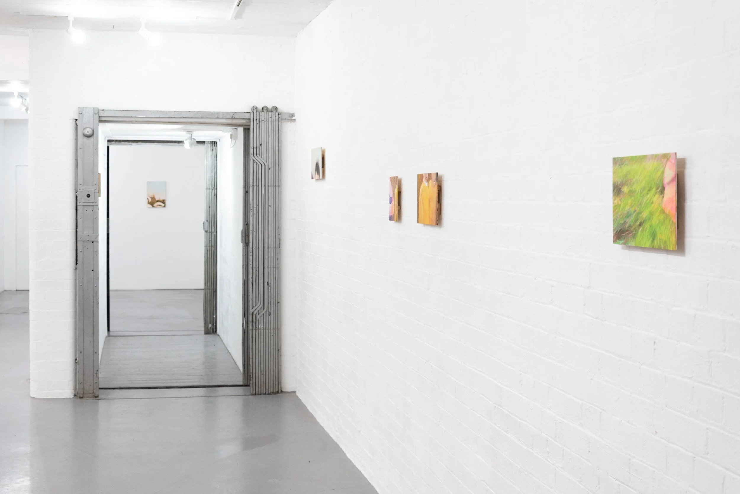 White gallery wall with small paintings and an industrial metal sliding door in an art gallery or studio.