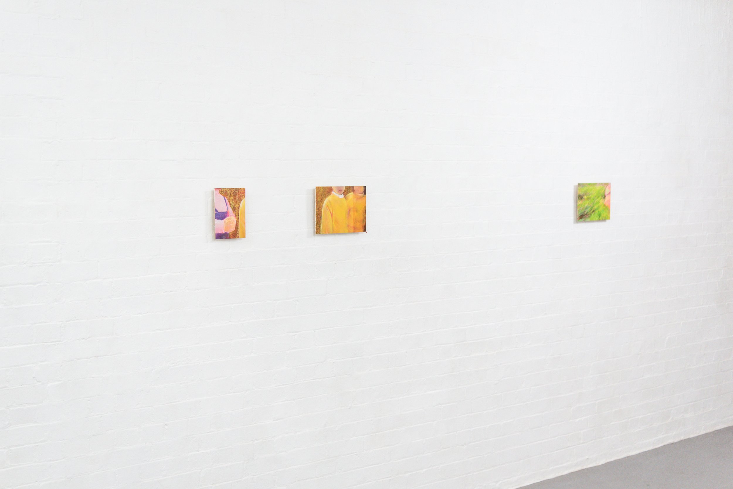 Three small paintings hung on a white brick wall in an art gallery.