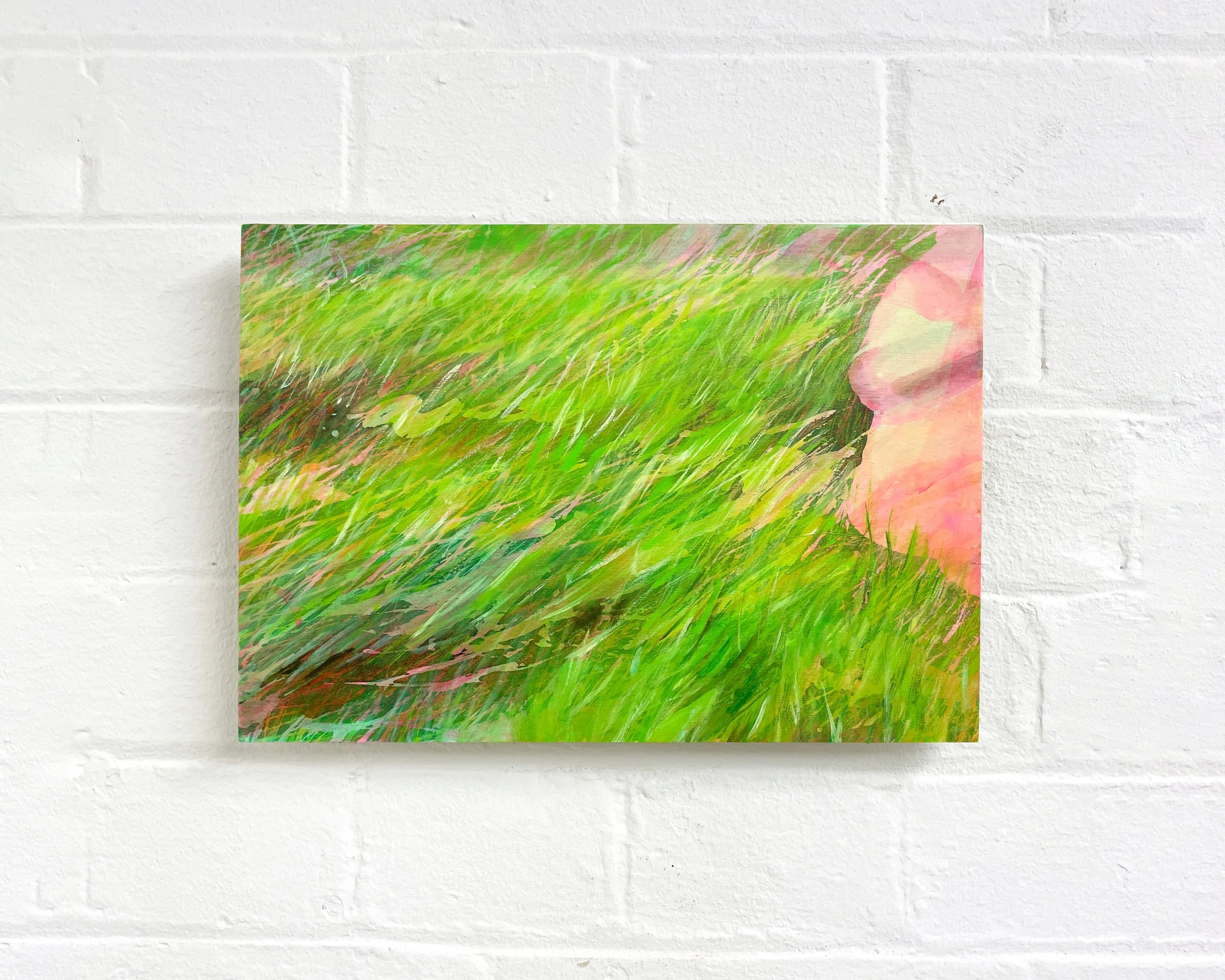 Close-up of a colorful abstract painting with green, pink, and yellow hues, mounted on a white brick wall.