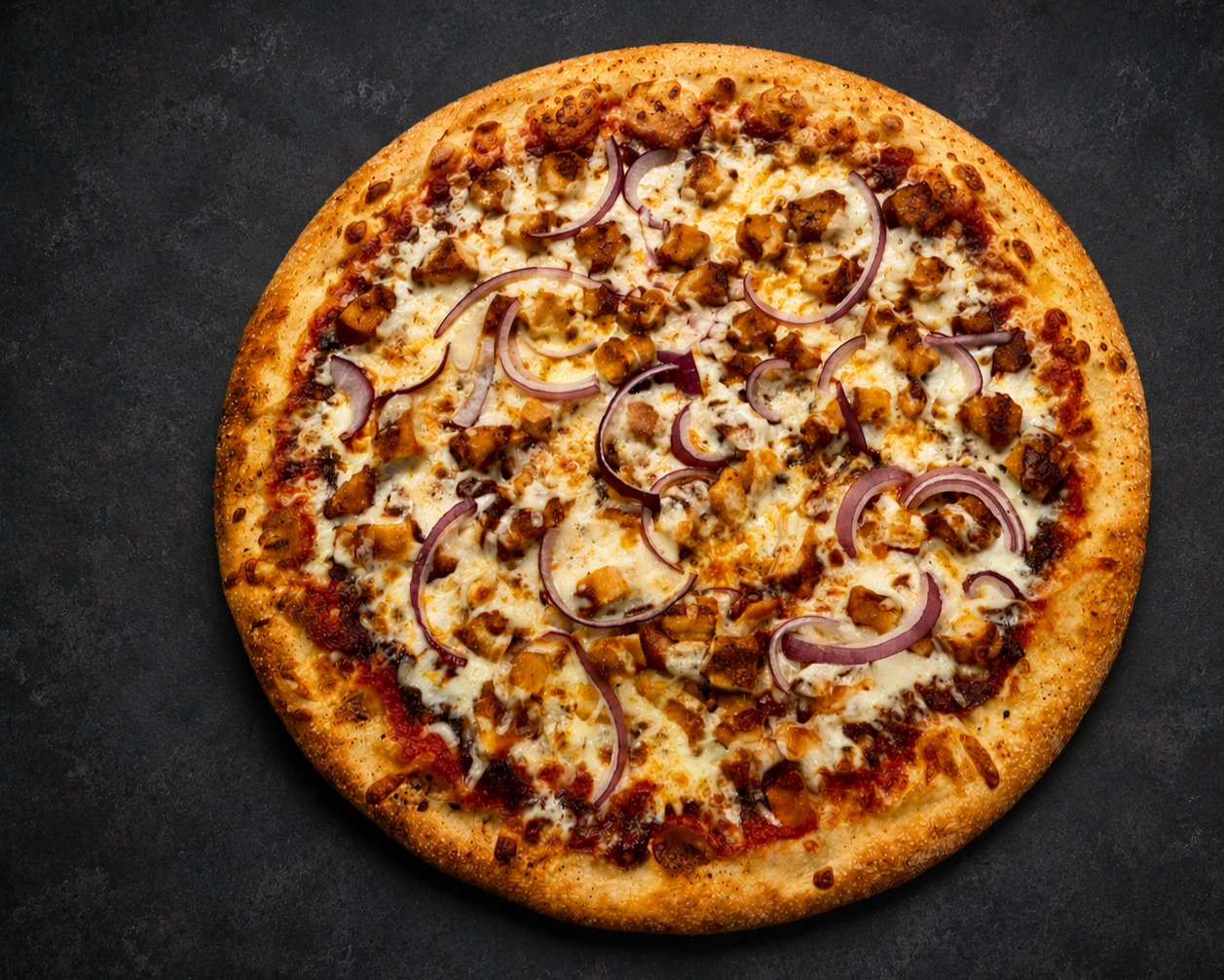 A whole pizza with cheese, chicken, and red onions on a dark surface.