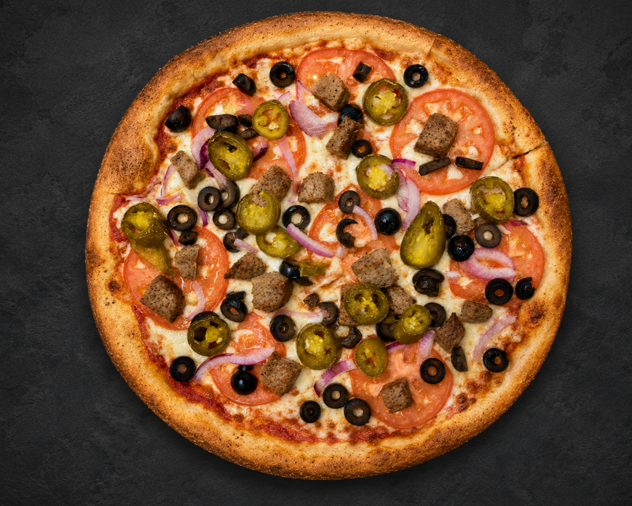 A pizza with cheese, sliced tomatoes, black olives, jalapenos, red onions, and chunks of sausage on a dark surface.