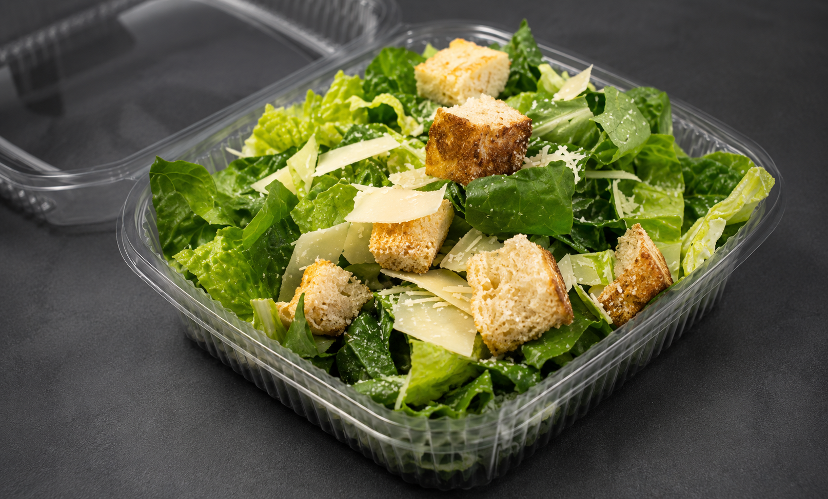 Green lettuce salad with shredded cheese and croutons in a clear plastic container.