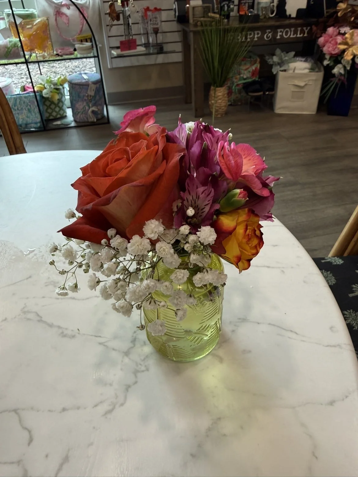 Un bouquet de fleurs colorées dans un vase vert, placé sur une table en marbre blanc à l'intérieur d'une boutique ou d'un magasin de fleurs.