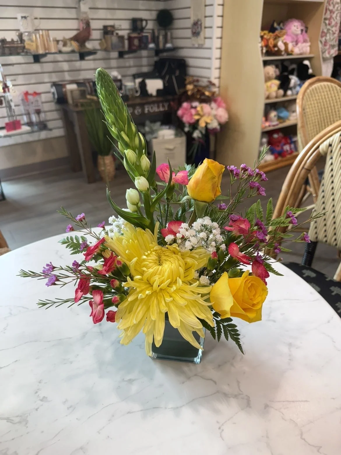 Un bouquet de fleurs colorées dans un vase en verre sur une table en marbre. Le bouquet comprend des fleurs jaunes, roses, blanches et violettes.