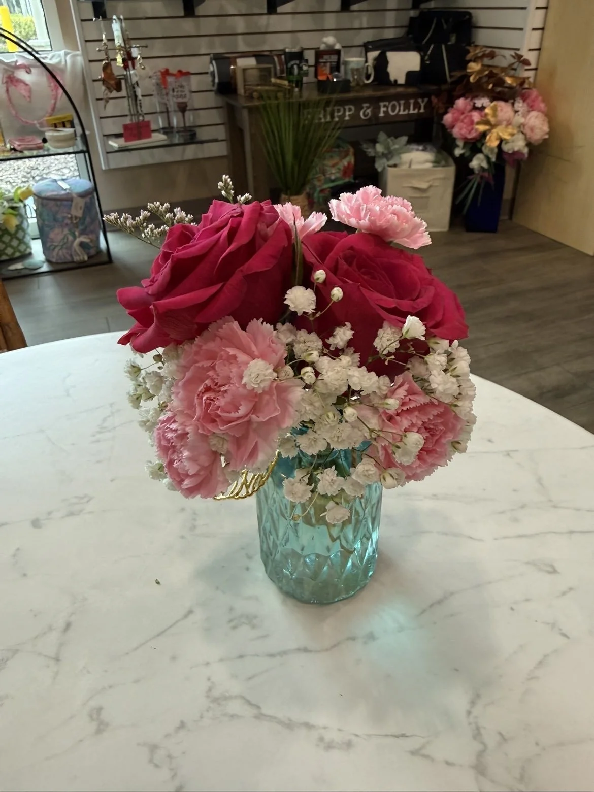 Un bouquet de fleurs roses et blanches dans un vase en verre bleu sur une table en marbre.