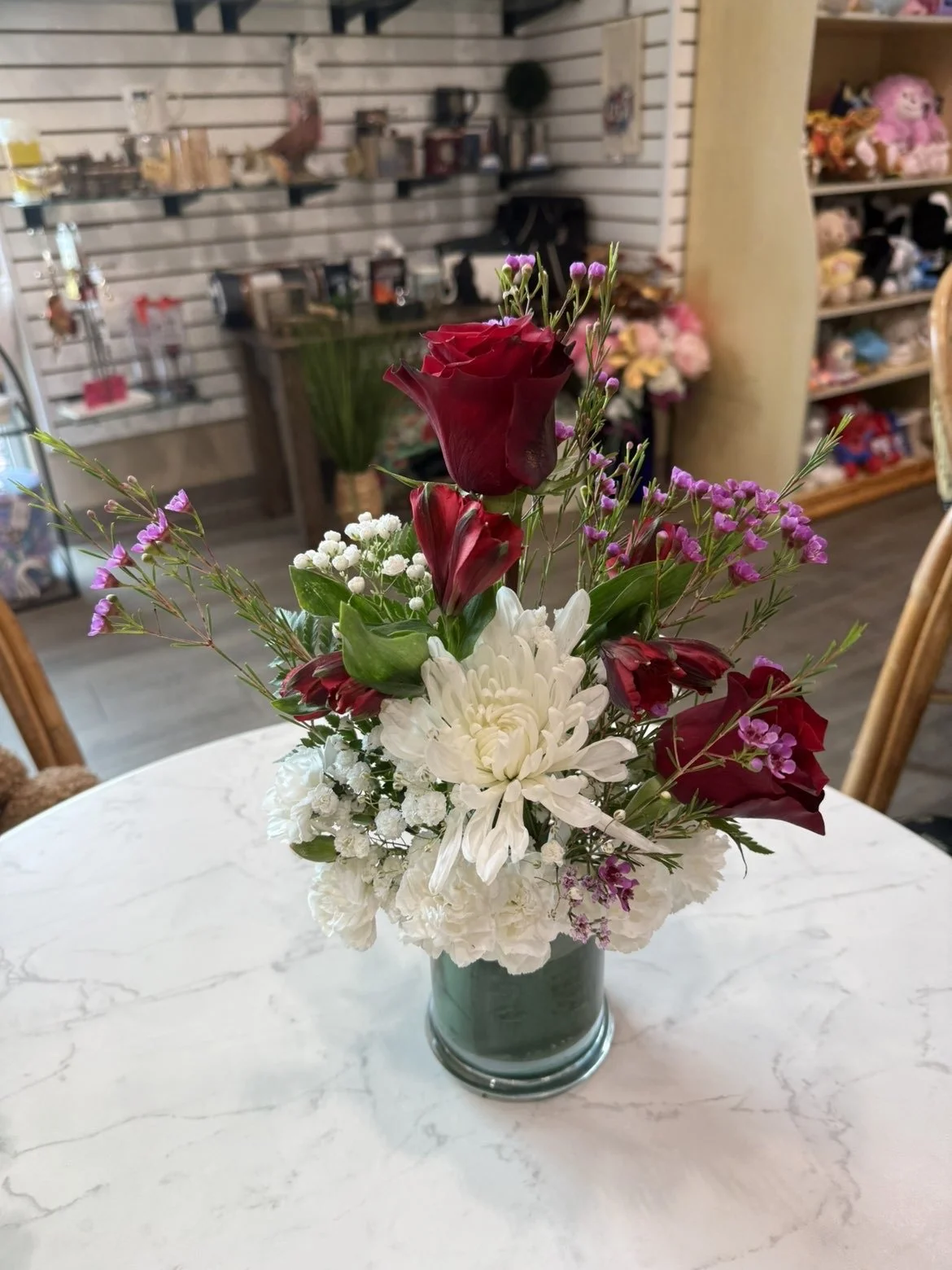 Un bouquet de fleurs dans un vase en verre, comprenant des roses rouges, des dahlias blancs, des petites fleurs violettes et blanches, placé sur une table en marbre.