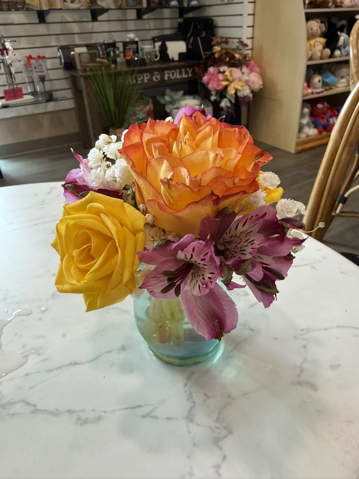 Un bouquet de fleurs avec des roses jaunes et un oiseau-orange, des alstroemerias violettes, dans un vase en verre sur une table en marbre.