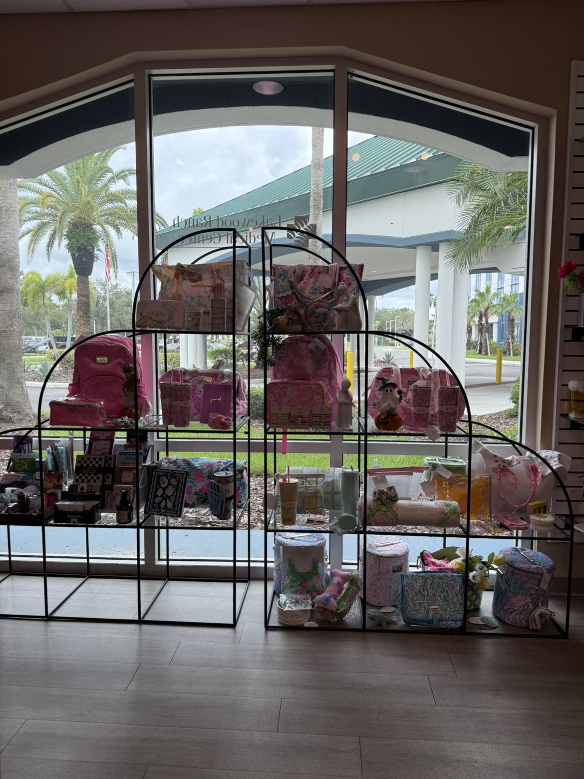 Vitrine de magasin avec des sacs à main, accessoires et décoration, vue à travers une grande fenêtre avec un extérieur tropical.