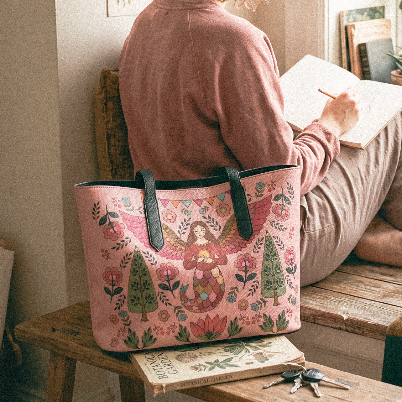 Artlen Studio pink tote bag featuring an original fairy and floral illustration, styled in a relaxed living room.