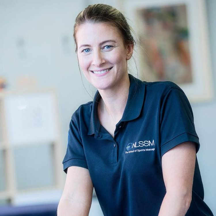 Smiling woman with brown hair tied back, wearing a navy blue polo shirt with the logo and text for NLSSM, in an indoor setting with blurred background.