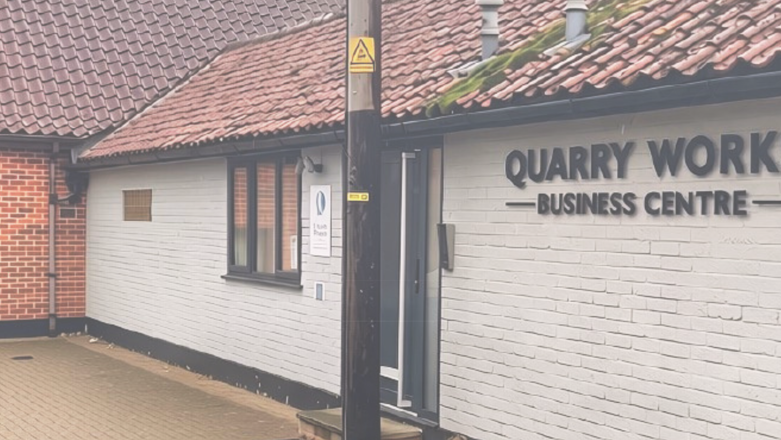 Street view of a quarry work business center with a white brick wall, sign, and a building with a tiled roof.