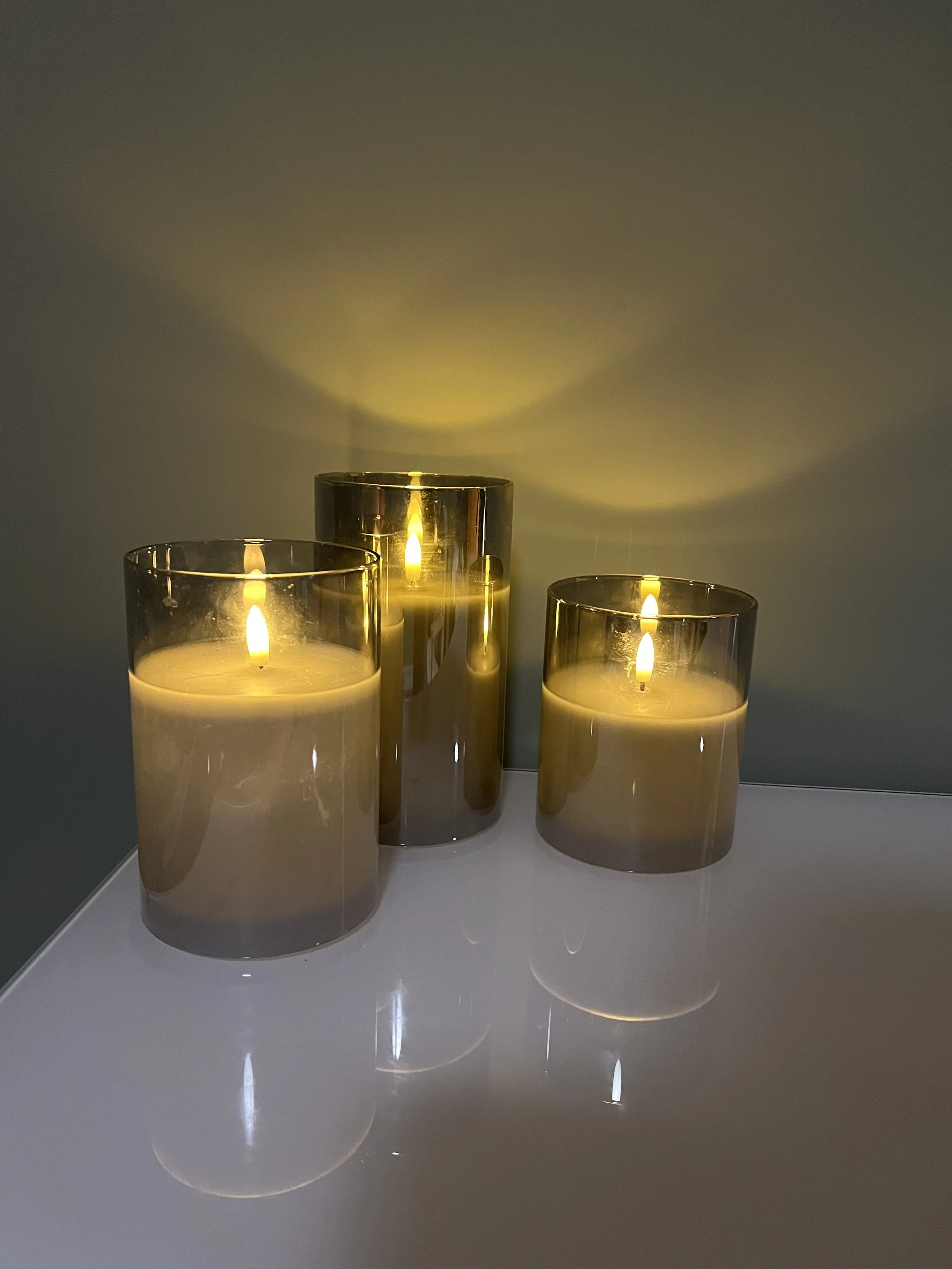 Four glowing candles in glass holders on a reflective tabletop