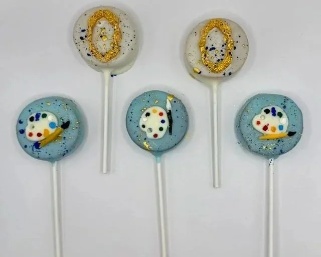 Handcrafted flat, round Luna Creations cake pops decorated with colorful artistic designs in blue, white, gold, black and red.