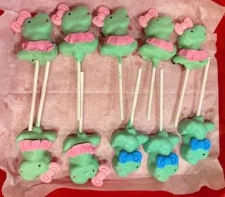 Handcrafted dinosaur-themed cake pops featuring T-Rex designs with colorful tutus and blue bows for a fifth birthday celebration.