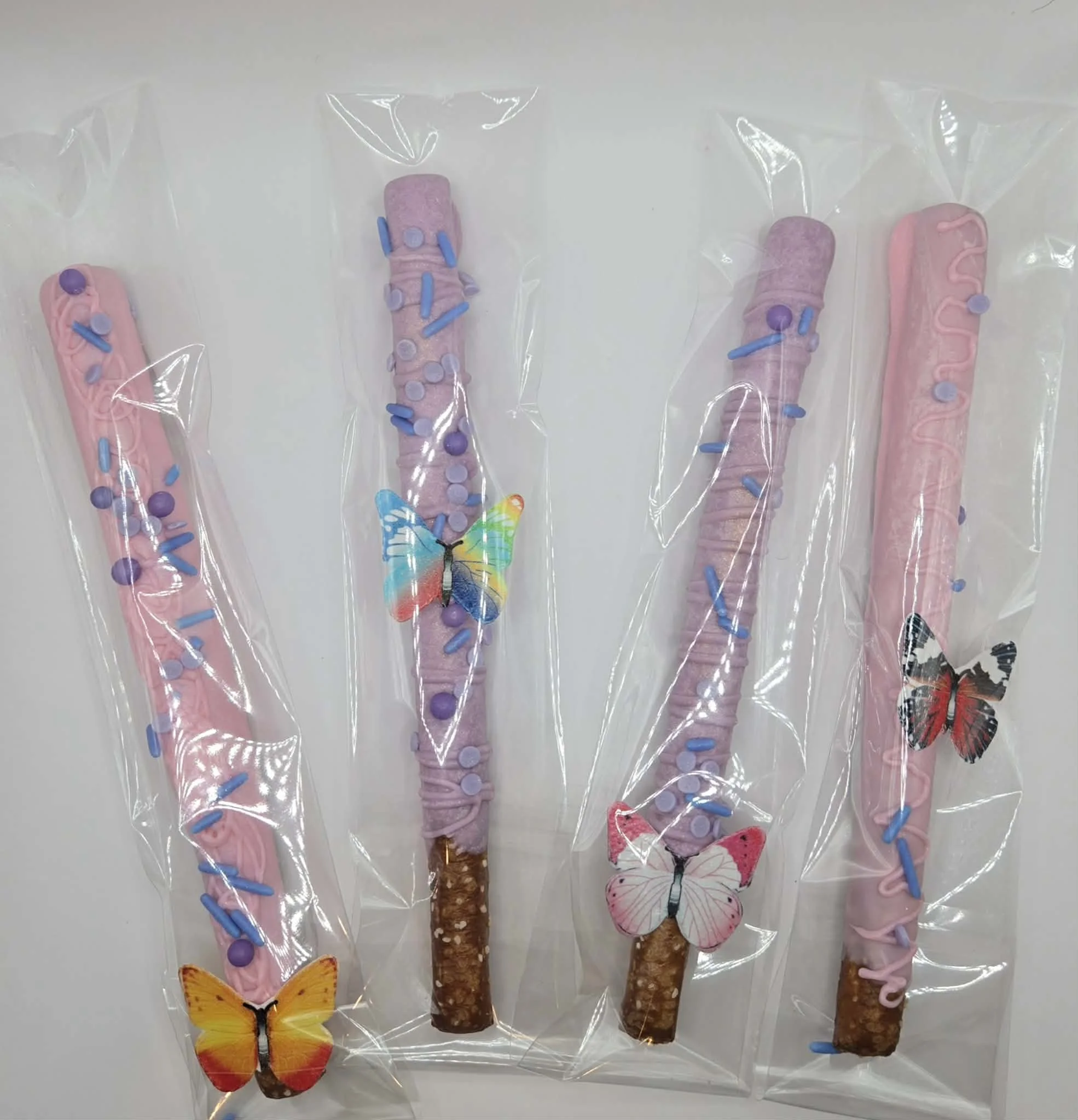 Individually wrapped chocolate-dipped pretzel rods decorated in pink, purple, and blue with whimsical fairy-themed butterflies for a seventh birthday celebration.