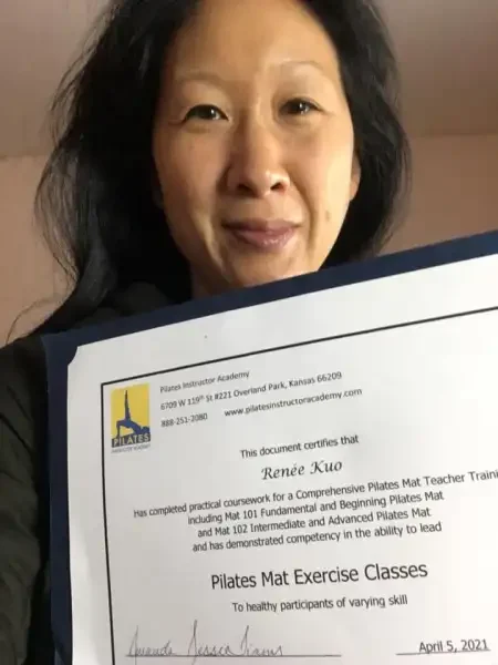 A woman holding a certificate from Pilates Instructor Academy, indicating she completed Pilates Mat Teacher training, dated April 5, 2021.