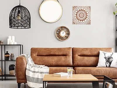 Cozy living room with a brown leather sofa, a wooden coffee table, wall decor, and a black hanging light fixture.