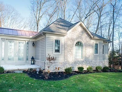 Front view of a suburban house with a stone facade and white siding, surrounded by a lawn and trees in the background.