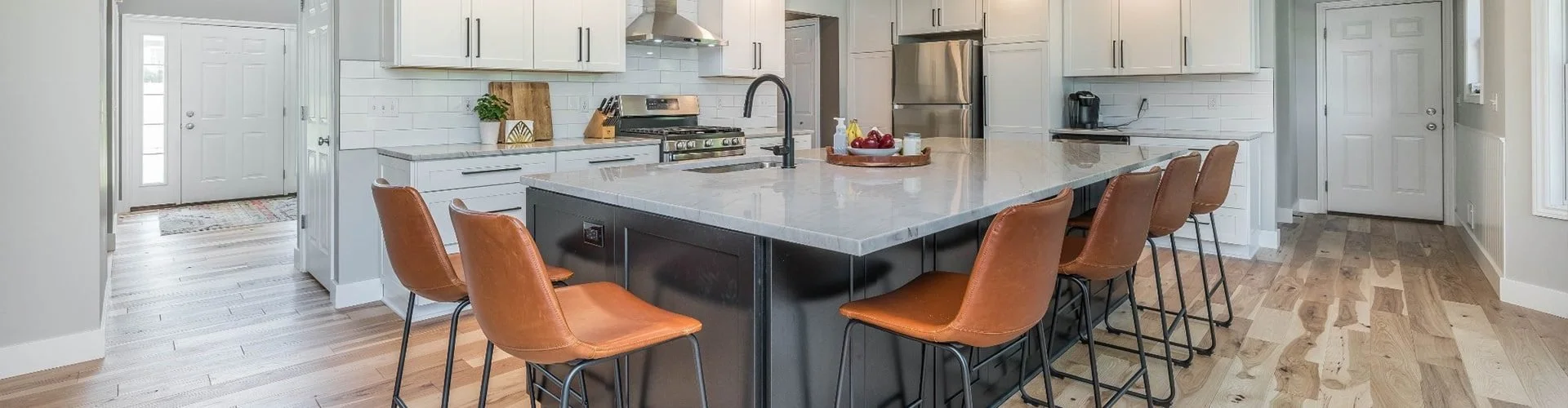 Modern kitchen with white cabinets, stainless steel appliances, and a kitchen island with brown leather chairs.
