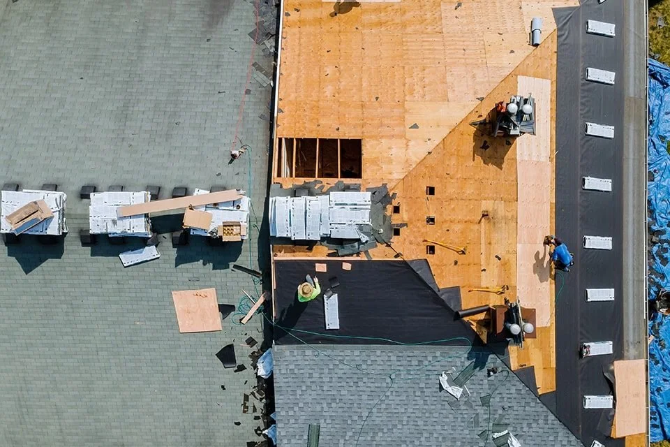 Aerial view of a construction site showing a partially built roof with workers working on it, roofing materials, and tools.