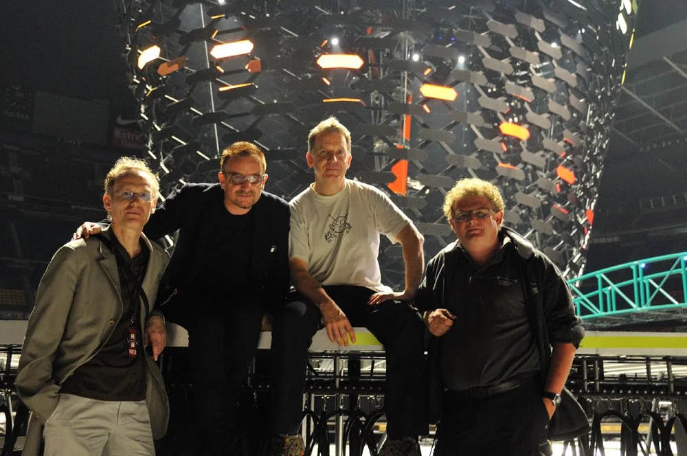 Four men standing in front of an elaborate stage setup with lighting and structural elements.