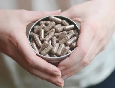 Person holding a metal tin filled with brown capsules or pills.