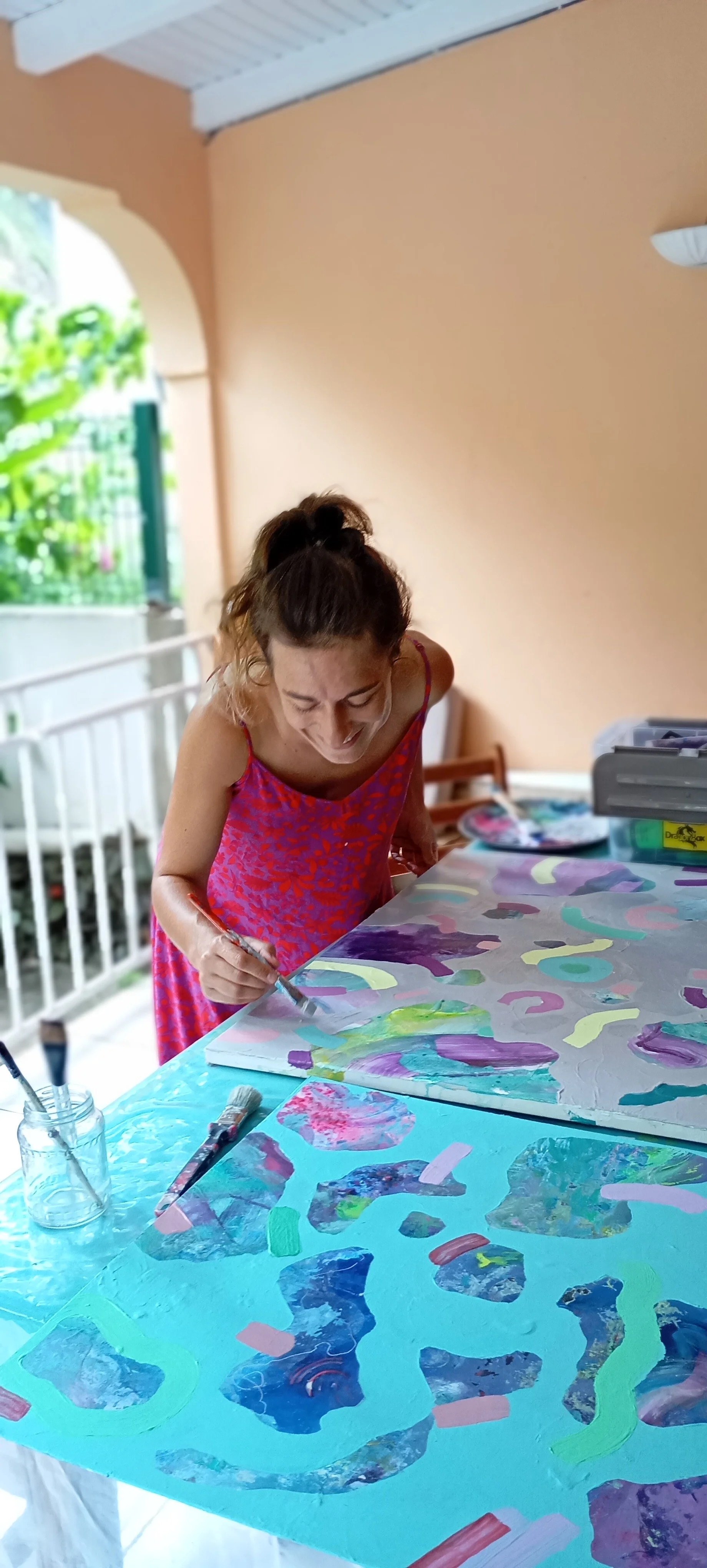 Une femme souriante en train de peindre une toile colorée dans un espace lumineux.