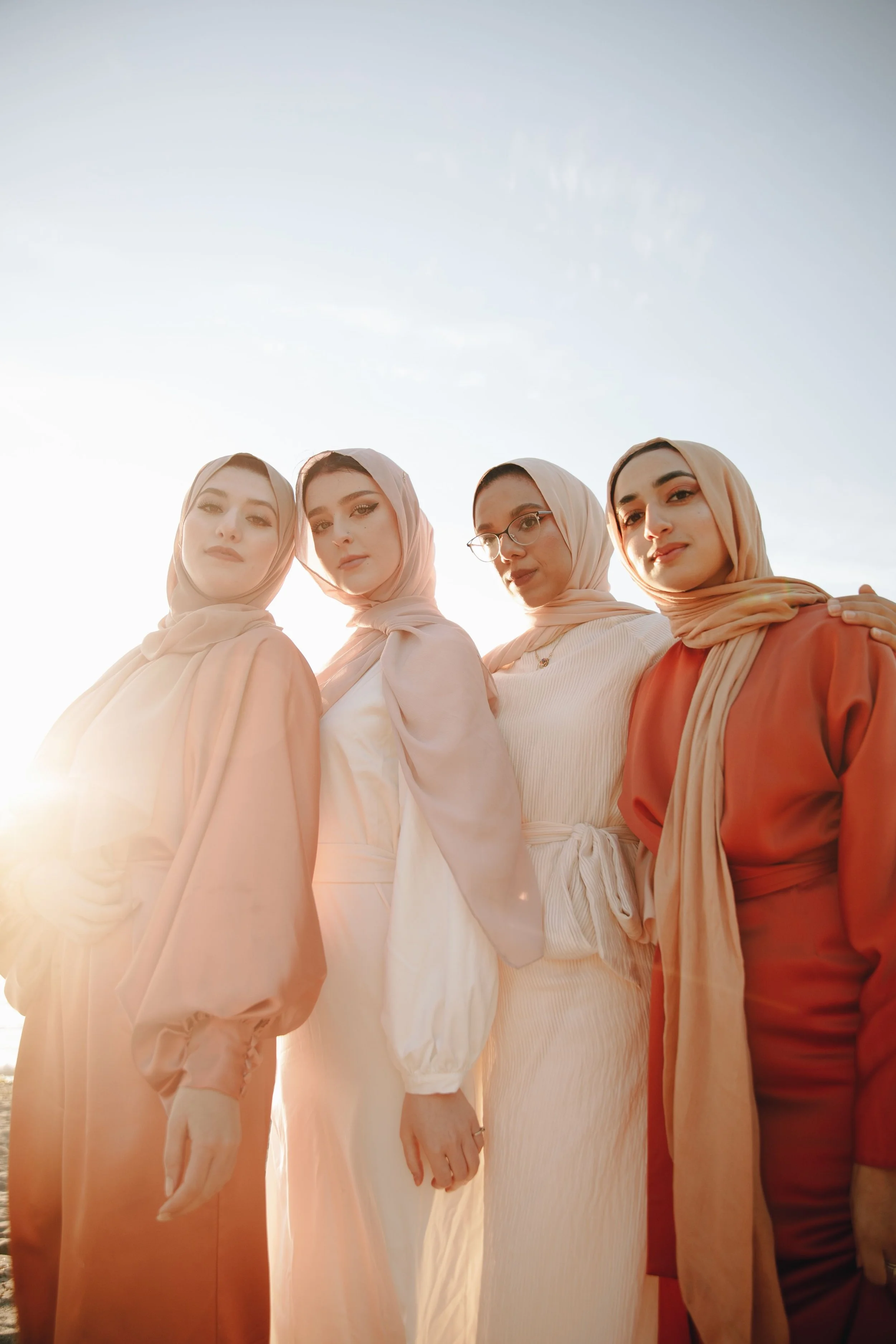 Four women wearing hijabs standing outdoors during sunset, with a clear sky behind them.