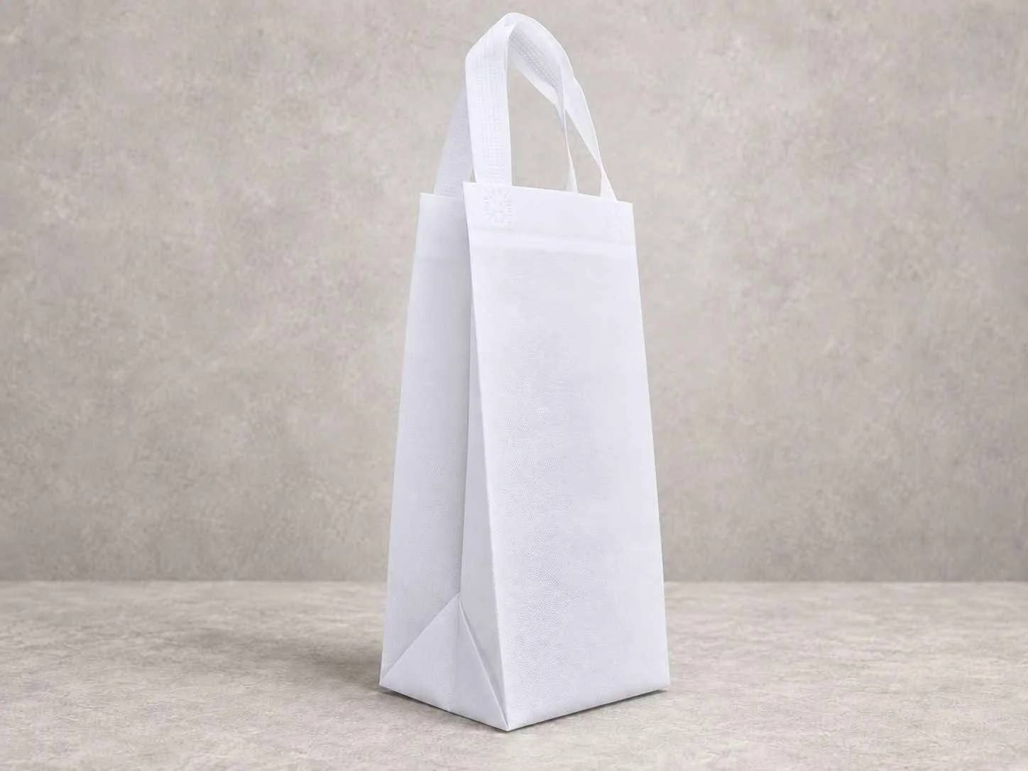 Empty white reusable shopping bag standing upright on a beige surface against a neutral background.