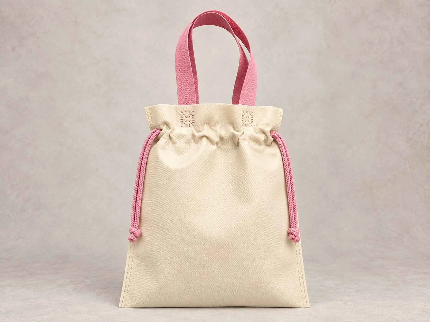 
Una bolsa reutilizable plana fusión color  marfil con cordón rosado de cambrel de pie vertical sobre una superficie neutra contra un fondo neutro.
