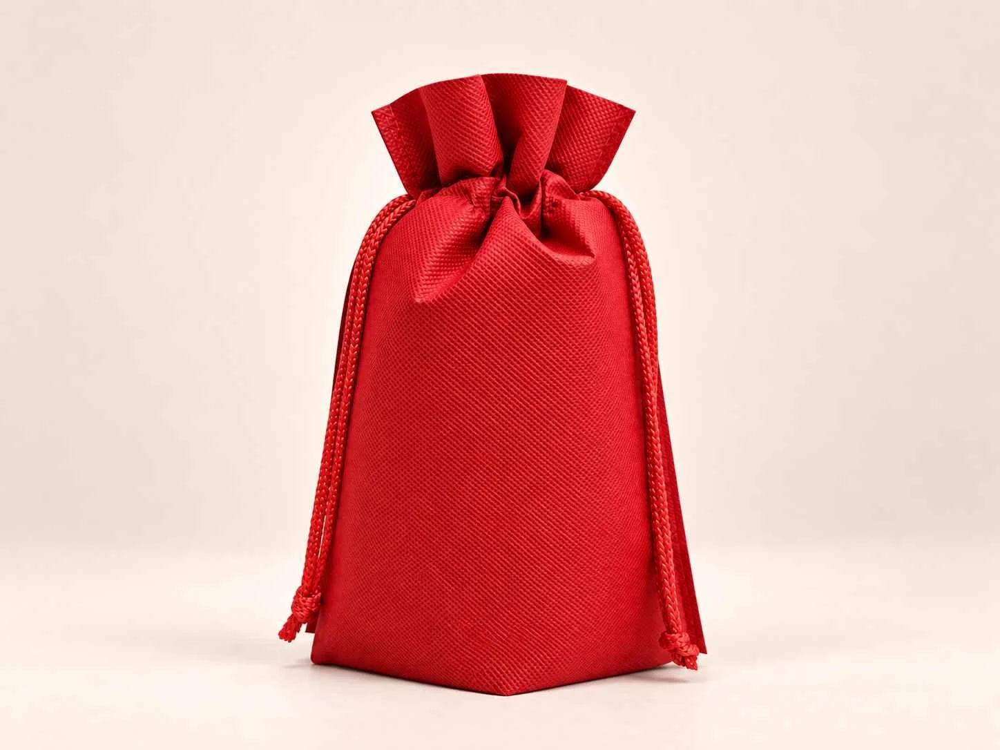 Bolsa en cambrel caramelo fuelle abajo reutilizable color rojo con cordones sobre un fondo neutro.