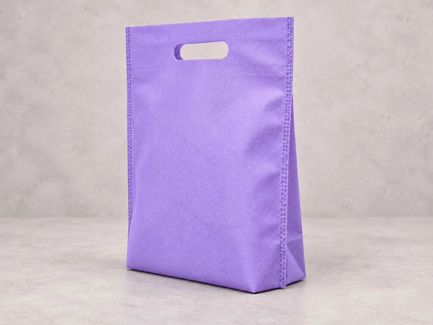 Purple reusable shopping bag con fuelle abajo standing upright on a light-colored surface against a neutral background.