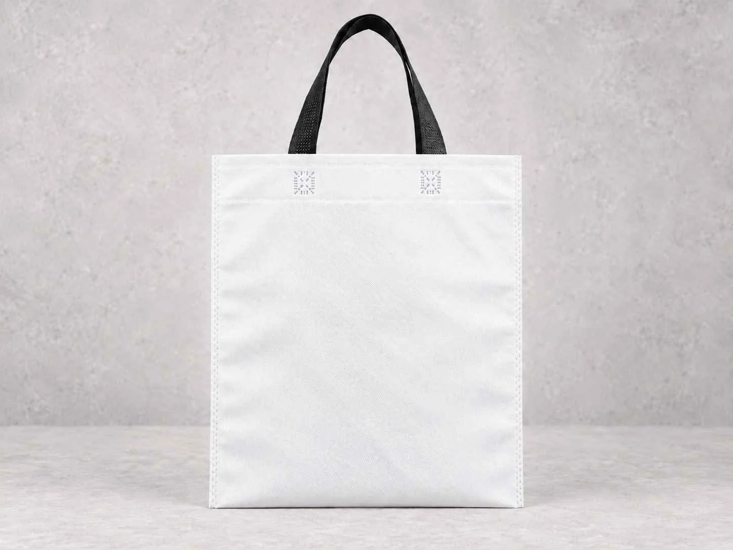 A white reusable shopping bag with black handles, placed against a neutral background.