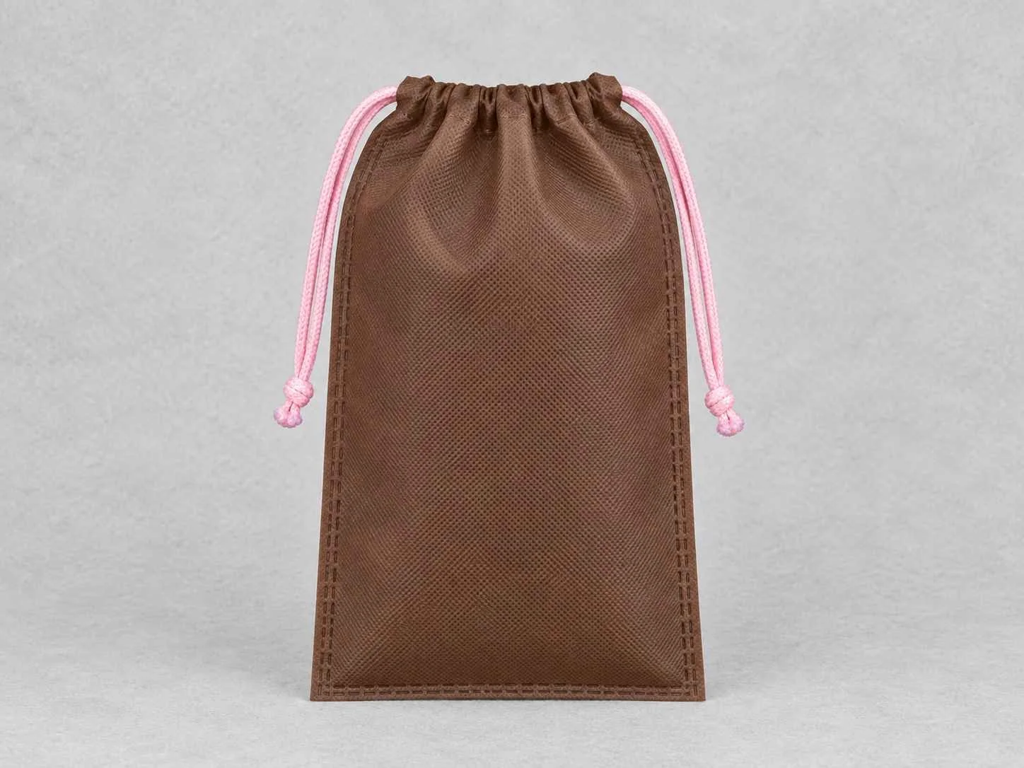 Brown cambrel bag with pink cords on a gray background.