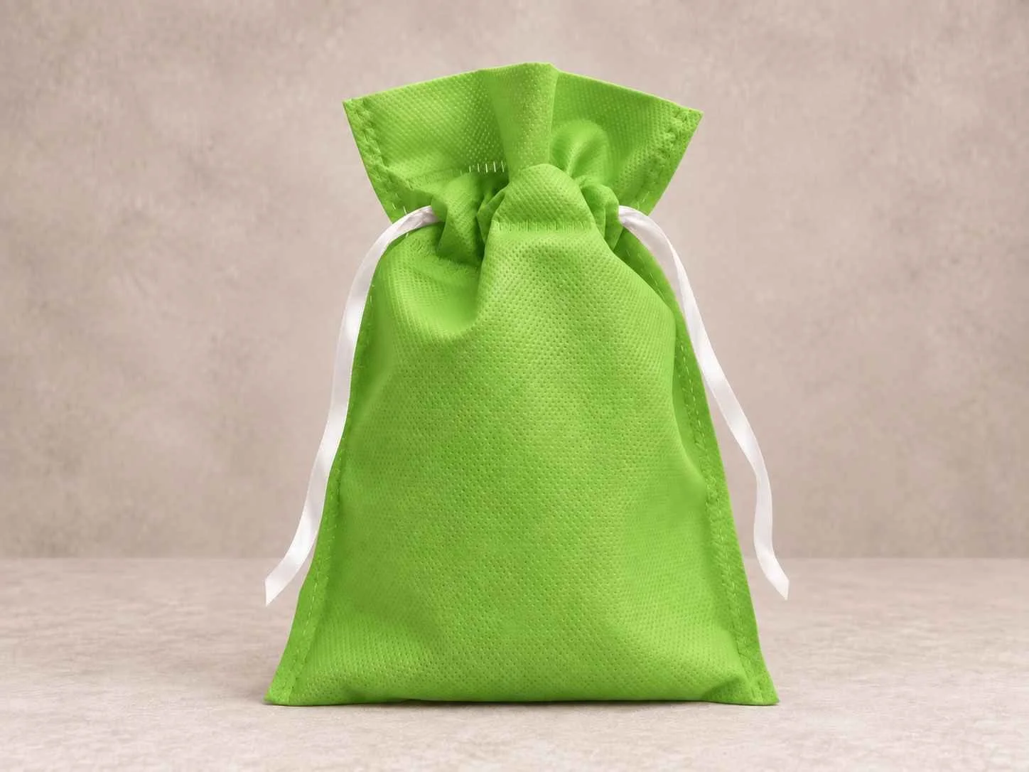Bolsa de cambrel reutilizable caramelo color verde manzana con cinta blanca sobre un fondo neutro.