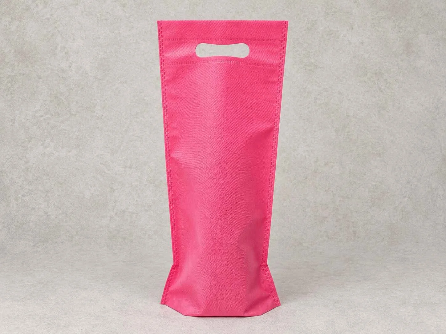 Pink plastic bag with a handle cutout, standing upright on a light gray surface.