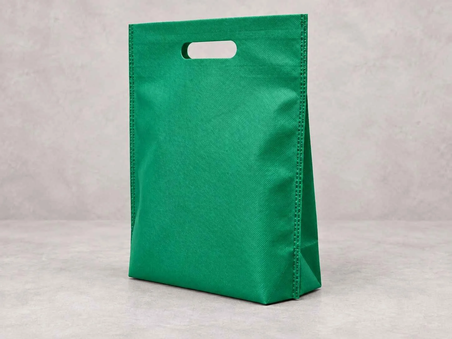 Bolsa en cambre verde plana con troquel y fuelle abajo on a neutral surface.