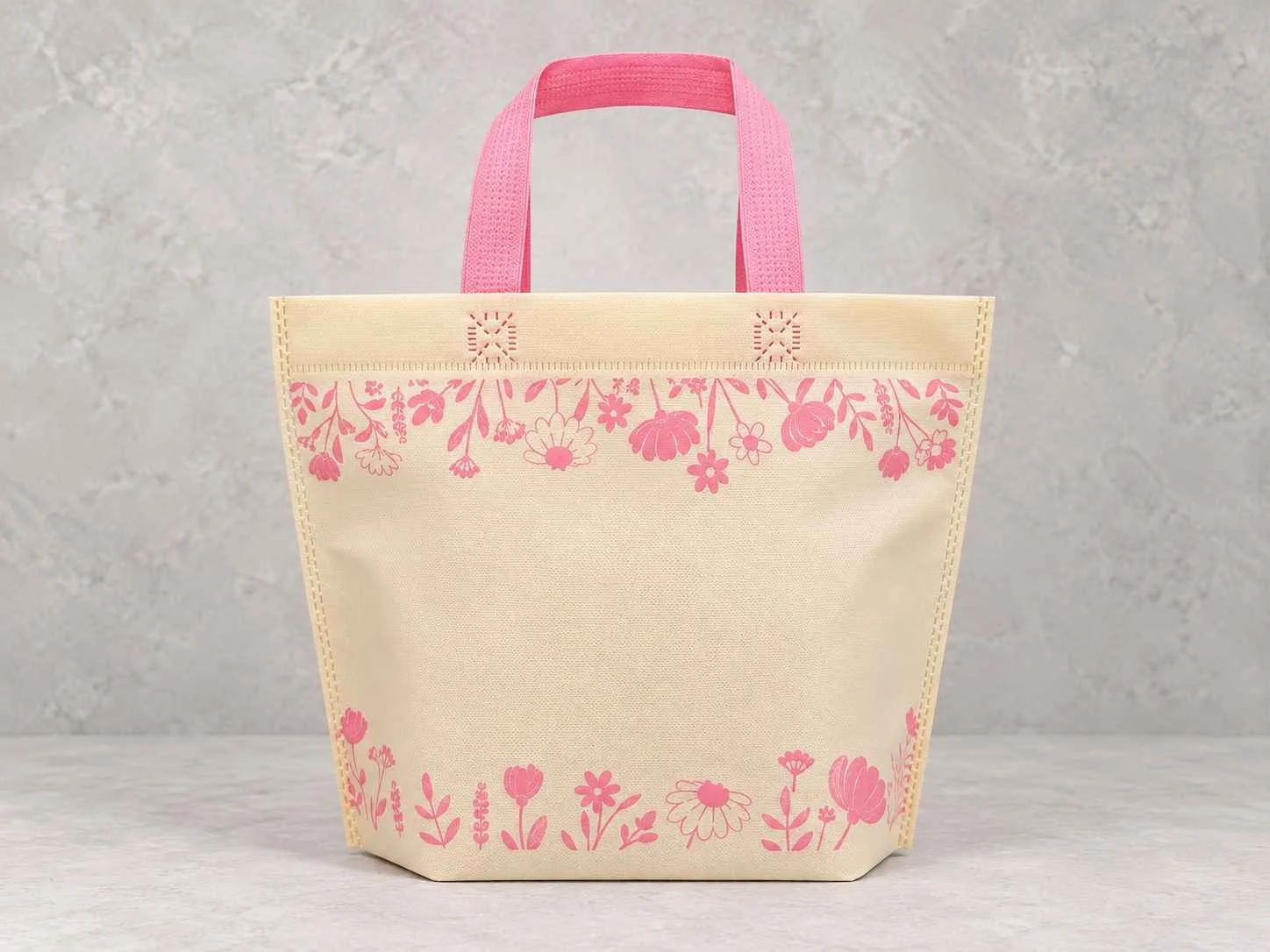 	
Bolsa de cambrel reutilizables manija plana con fuelle abajo color marfil con manijas rosadas con estampado de flores, sobre un fondo neutro.