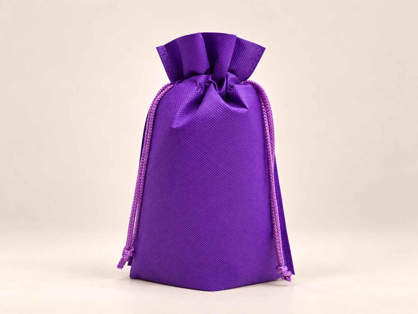 Bolsa en cambrel caramelo ajustable fuelle abajo reutilizable color morada con cordones sobre un fondo neutro.